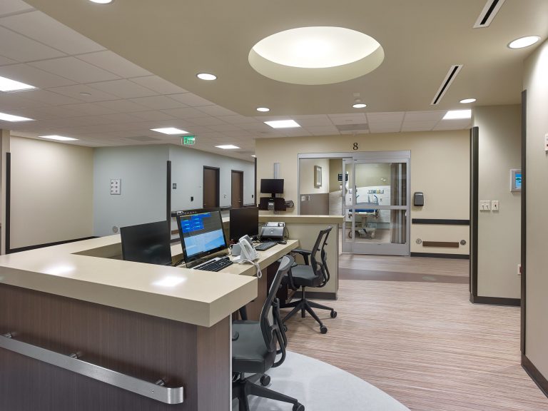 Poste de soins infirmiers moderne avec ordinateurs et accès aux chambres des patients.
