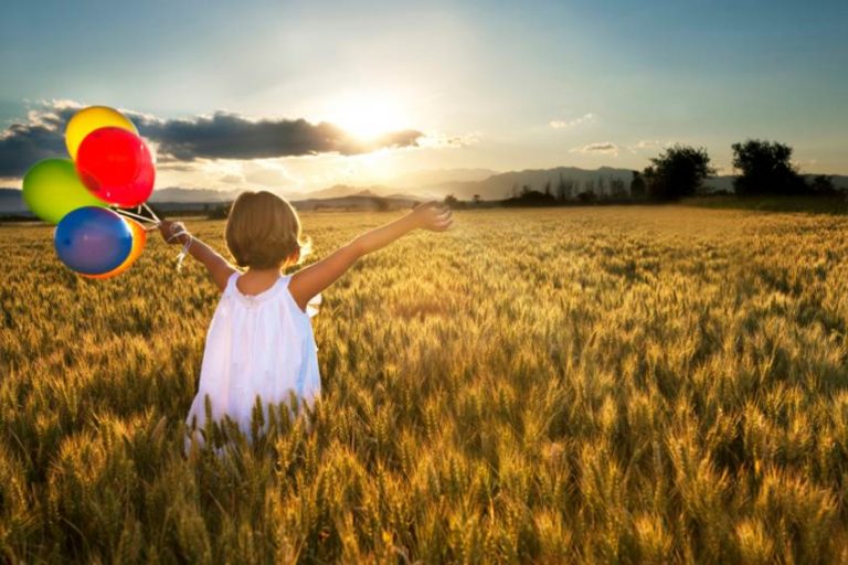 Fille dans un champ au coucher du soleil, les bras tendus, tenant des ballons colorés. Concept de luminothérapie naturelle.