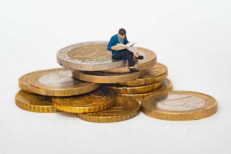 Homme miniature lisant sur une pile de pièces en euros.